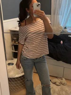 Randig offshoulder t-shirt - Självklippt!! Säljer en avslappnad t-shirt med rosa och vita ränder. Modellen är offshoulder med korta ärmar och har en loose passform. Perfekt för en chill och trendig look. Materialet känns mjukt och skönt, troligtvis bomull.
