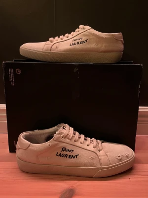 Saint Laurent vita canvas sneakers - Snygga vita sneakers från Saint Laurent i canvas med handskriven logga på sidan. Klassisk låg modell med rund tå och vita snören. Perfekta för en avslappnad och trendig look.