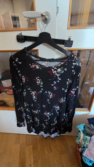 Svart blommig långärmad klänning - Svart klänning med blommigt mönster i rosa, vitt och grönt. Långärmad modell med rund halsringning och mjukt, stretchigt material. Perfekt för dig som gillar en romantisk och avslappnad stil.