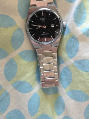 Tissot PRX Powermatic 80 klocka - Snygg Tissot PRX Powermatic 80 med svart urtavla och datumvisning. Klockan har ett stilrent armband i rostfritt stål och safirglas. Perfekt accessoar för dig som gillar klassisk och modern design.