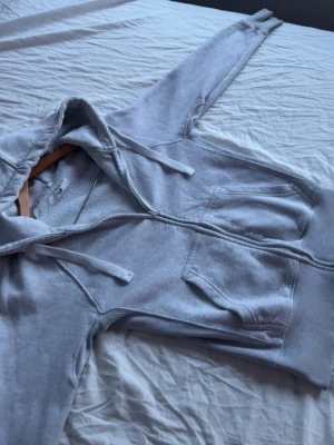 Russemerch tröja - Ljusgrå hoodie med dragkedja och stora framfickor. Modellen har huva med dragsko och ribbade muddar vid ärmslut och nederkant. Perfekt för en avslappnad och chill stil.