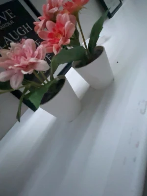 Två rosa konstblommor i vita krukor - Säljer två konstgjorda blommor med rosa och ljusrosa kronblad i vita krukor. Bladen är gröna och blommorna har en naturlig look som passar perfekt som dekoration i hemmet. Krukorna är enkla och stilrena.