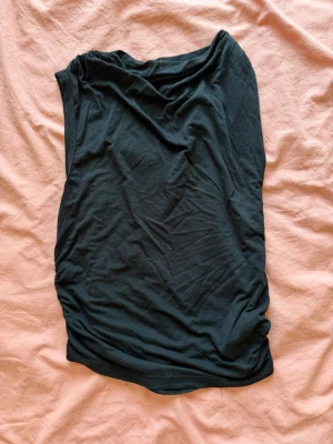 Svart ärmlös topp med draperad hals - En svart ärmlös topp med snygg draperad halsringning. Toppen har en enkel och stilren design, perfekt att matcha med jeans eller kjol. Tillverkad i mjukt material som känns skönt mot huden.