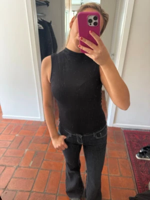 Svart ärmlös polotopp - Snygg svart ärmlös polotopp med tight passform. Perfekt att styla med jeans eller kjol för en clean look. Hög hals och mjukt material som sitter skönt mot kroppen.