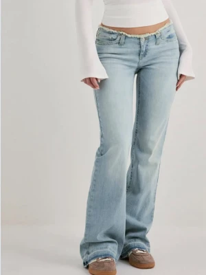 Ljusblå bootcut jeans med rå kant från Nelly  - Snygga ljusblå bootcut jeans med låg midja och rå, fransad kant upptill. Jeansen har klassisk femficksdesign och är tillverkade i mjuk denim med lite stretch för skön passform. Perfekta för en avslappnad och trendig look. Storlek EU34
