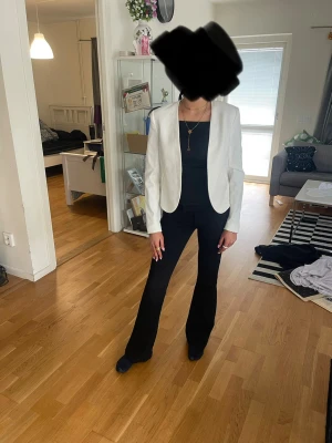 Vit figursydd kavaj - Snygg vit kavaj med figurnära passform och öppen front. Kavajen har långa ärmar och en stilren, minimalistisk design som passar perfekt till både jeans och kostymbyxor. Materialet ser ut att vara ett slätt tyg, troligen polyesterblandning.