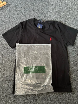 Svart t-shirt från Polo Ralph Lauren - Svart t-shirt från Polo Ralph Lauren med klassisk röd broderad logga på bröstet. T-shirten har rund halsringning och korta ärmar. Tillverkad i mjuk bomull för en skön känsla och stilren look. S/XS