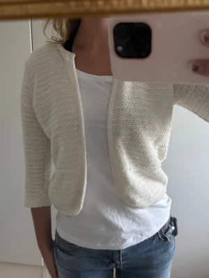 Vit stickad kofta med trekvartsärm/ bolero  - Säljer ett par ljusblå jeans med bootcut-passform. Jeansen har klassisk femficksdesign och normalhög midja. Materialet är denim och färgen har en lätt tvättad look som ger en avslappnad vibe.