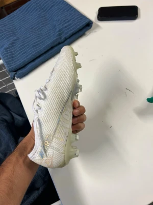 Nike Mercurial vita fotbollsskor - Säljer ett par vita Nike Mercurial fotbollsskor med silvriga detaljer och snörning. Skorna har en lätt och smidig ovandel i syntetmaterial och mönstrad yta för bättre bollkontroll. Perfekta för dig som vill ha snabbhet och stil på planen. Storlek 39! Använda ett par gånger men säljs inte alls. Väldigt sällsynta och eftersökta. Pris går att diskutera!