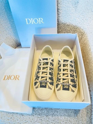 Dior Oblique låga sneakers - Snygga Dior Oblique sneakers i canvas med klassiskt blått och vitt monogrammönster. Låg modell med vita snören och gummisula där 'Christian Dior' är präglat baktill. Perfekta för dig som vill ha en lyxig och trendig look. Köpte dessa förra året och är i nästan ny stick har andvänds sparsamt och behövs inte mer. Vill du se mer bilder så fråga Järna 