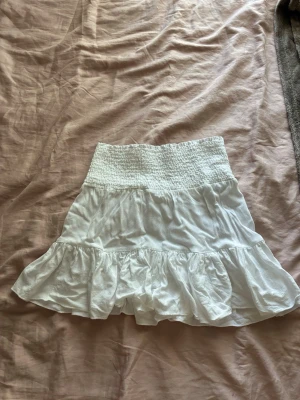 Vit volangkjol  - Söt vit kortkjol med bred smock i midjan och volangdetaljer. Kjolen har en luftig och flowy känsla. Tillverkad i ett mjukt tyg. Använt några gånger 