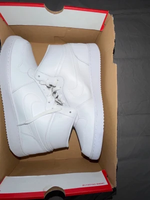 Nike sneakers - Säljer ett par helvita Nike sneakers i high-top modell. Skorna har klassisk Nike Swoosh på sidan, vita skosnören och är tillverkade i slätt läder. Perfekta för dig som gillar stilrena och tidlösa sneakers med en sportig vibe.