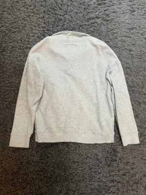 Ljusgrå halvzip sweatshirt från lager 157 - Ljusgrå sweatshirt med halv dragkedja och hög krage från lager 157. Tröjan har långa ärmar, ribbade muddar och en avslappnad passform. Perfekt för en chill och stilren look.