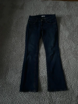 Mörkblå bootcut jeans - Snygga mörkblå bootcut jeans med klassisk femficksdesign och kontrastsömmar. Jeansen har utsvängda ben och låg midja, perfekta för en trendig och avslappnad look. Tillverkade i denim med lätt stretch för extra komfort.