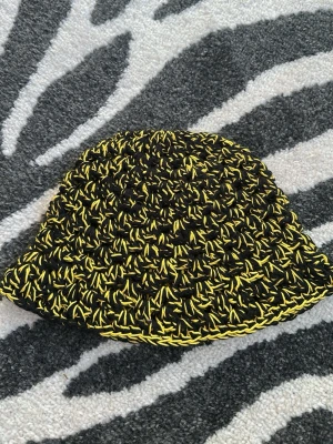 Svart och gul virkad bucket hat - Unik handvirkad bucket hat i svart och gult bomullsgarn. Sitter bra på mig med 55cm i omkrets på huvudet.