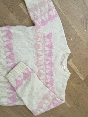 Vit och rosa stickad tröja Gina Tricot - Mysig stickad tröja från Gina Tricot i vitt med ljusrosa mönster. Tröjan har rund halsringning, långa ärmar och ribbade muddar. Perfekt för kalla dagar och har ett gulligt hjärtmönster som ger en söt touch.