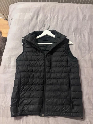 Svart dunväst från Peak Performance - Snygg svart dunväst från Peak Performance med quiltad design och dragkedja framtill. Västen har hög krage, två sidofickor med dragkedja och en bröstficka. Perfekt för lager-på-lager och håller dig varm under kyliga dagar. Ingen skada på den osv! Nypris 1899 kr!