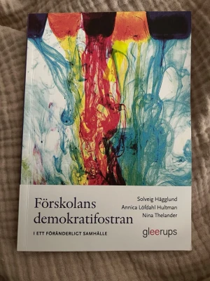 Förskolans demokratifostran - Kursbok om förskolans roll i demokratifostran, skriven av Solveig Hägglund, Annica Löfdahl Hultman och Nina Thelander. Omslaget har färgstarka abstrakta mönster i blått, rött, gult och svart. Perfekt för dig som pluggar pedagogik eller förskollärarutbildning.