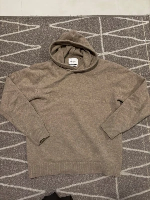 Beige hoodie i merinoull från Vailent - Säljer en stilren beige hoodie från Vailent i mjuk merinoull. Hoodien har ribbade muddar vid ärmslut och nederkant samt en klassisk huva. Perfekt för dig som gillar en clean och avslappnad look.