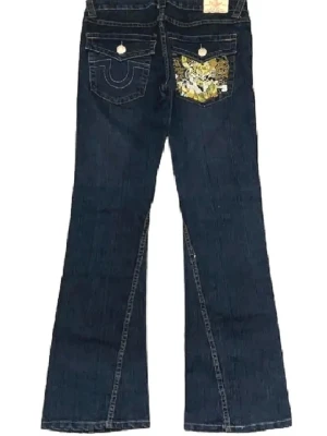 True Religion Jeans - Snygga mörkblå bootcut jeans från True Religion med klassiska kontrastsömmar och detaljerade bakfickor, varav en har ett gult mönster. Jeansen har låg midja och gylf med knapp. Perfekta för dig som gillar en avslappnad men trendig look.