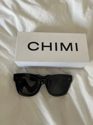 Svarta solglasögon från CHIMI - Stilrena svarta solglasögon från CHIMI med bred båge och fyrkantig form. Kommer med originaletui och förpackning. Perfekta för att lyfta din look med en modern och trendig vibe.