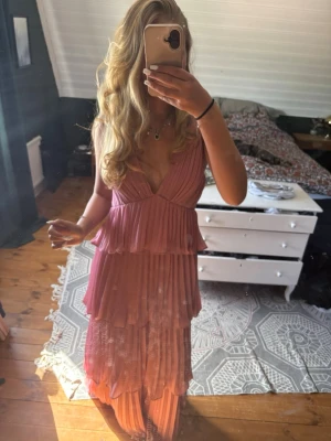 Lulus balklänning  - Säljer en lång, rosa klänning med flera lager volanger och djup v-ringning. Klänningen är ärmlös, har öppen rygg med knyt i nacken och är tillverkad i ett lätt, plisserat material som ger ett flowy intryck. Perfekt för balen, säljee pågrund av den är för stor för mig💞