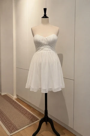 Vit axelbandslös kort klänning - Säljer en elegant vit axelbandslös klänning med draperad överdel och lätt utställd kjol. Klänningen har en mjuk, flowy känsla och är perfekt för sommarens alla tillfällen och studenten!! 💞