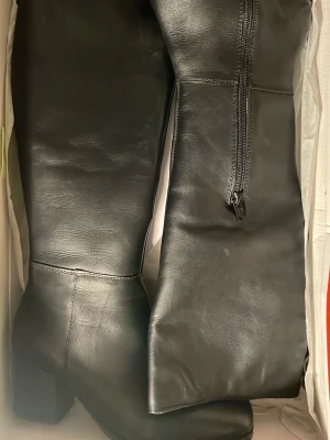 Svarta knähöga skinn stövlar med klack - Säljer ett par stilrena svarta knähöga stövlar från London Rebel!! De har en markerad blockklack och dragkedja på insidan för enkel påtagning. Överdelen är skinn medan sulan är gummi. 