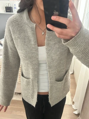 Stickad kofta  - Fin grå stickad kofta med två fickor framtill. Enkel och snygg att ha till vardagliga outfits eller över en klänning i sommar!