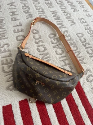 Louis Vuitton Monogram axelväska - Säljer en snygg axelväska från Louis Vuitton i klassiskt brunt monogrammönster. Väskan har justerbar beige axelrem i läder, guldfärgade metalldetaljer och präglad logotyp på handtaget. Perfekt för dig som gillar lyxiga accessoarer och tidlös design.