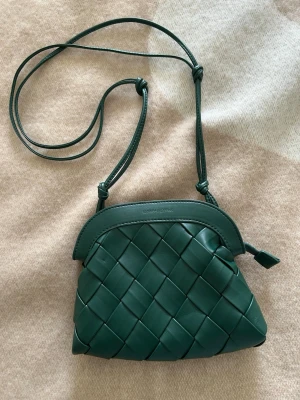  Ny Grön axelväska från Carin Wester  - Snygg grön axelväska från Carin Wester i flätad läderdesign. Väskan har justerbar axelrem med knutar och dragkedja upptill. Insidan är fodrad i tyg och har en liten innerficka. Perfekt för dig som gillar stilrena detaljer och exklusivt material. Ny oanvänd 
