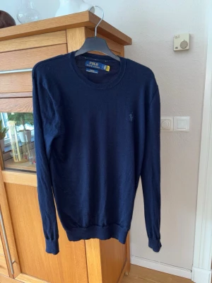 Mörkblå stickad tröja Polo Ralph Lauren - Klassisk mörkblå stickad tröja från Polo Ralph Lauren i tunn merinoull. Storlek S. Har ett litet hål på ena ärmen, men inget man generellt tänker på och går dessutom att sy igen. 