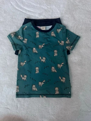 Grönt set med hundmönster - Sött set med en grön kortärmad body med mörkblå kant och gulligt hundmönster samt matchande mörkblå shorts. Perfekt för dig som gillar lekfulla och bekväma plagg. Materialet känns mjukt och skönt mot huden.