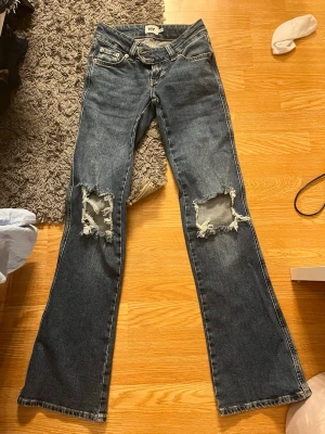 Mörkblå bootcut jeans med slitningar - Säljer ett par mörkblå bootcut jeans från 157 med stora slitningar över knäna. Jeansen har klassisk femficksmodell, låg midja och råa kanter vid hålen. Perfekta för en avslappnad och trendig look.