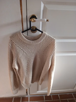 Beige stickad tröja med strukturmönster - Säljer en beige stickad tröja med snyggt strukturmönster och rund hals. Tröjan har långa ärmar och ribbade muddar vid hals, ärmslut och nederkant. Perfekt för lager på lager och riktigt mysig till hösten och vintern.