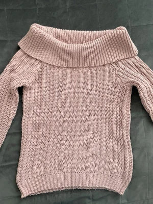 Ljusrosa off shoulder stickad tröja - Säljer en ljusrosa stickad tröja i off shoulder och ribbstickad struktur. Tröjan har långa ärmar och är perfekt för dig som vill ha något i skolan eller jobbet. Väldigt stilren och trendig i modet. Materialet känns mjukt och mysigt. Passar till jeans, kostymbyxor eller kjol. 