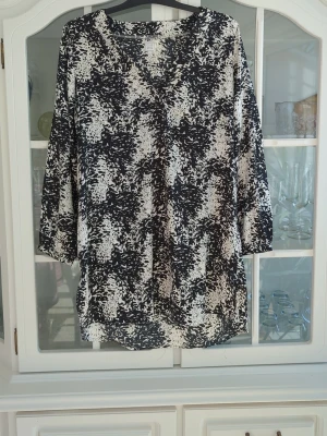 Svartvit mönstrad blus med V-ringning - Svartvit blus med abstrakt mönster och V-ringning. Blusen har trekvartsärm och en lös, avslappnad passform. Perfekt för dig som gillar en stilren men ändå unik look. Tillverkad i ett lätt och mjukt tyg som känns skönt mot huden.