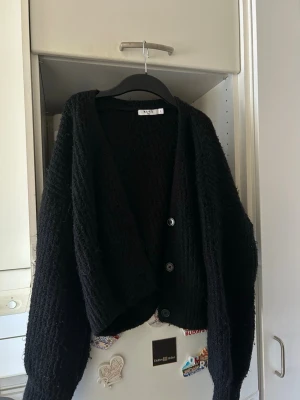 Svart kofta från NA-KD med knappar - Mysig svart kofta från NA-KD med tre  knappar. Koftan har en avslappnad passform