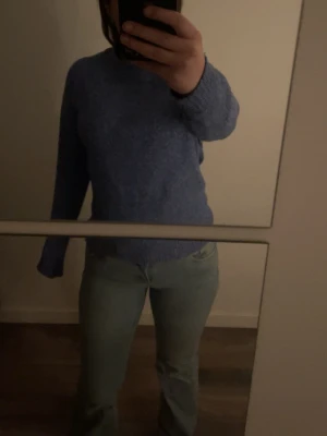 Blå stickad tröja med rund hals - Mysig blå stickad tröja med rund hals och långa ärmar. Tröjan har ribbstickade muddar vid ärmslut och nederkant. Perfekt för kyligare dagar och enkel att matcha med jeans eller kjol. Knarr använd och väldigt mysig!