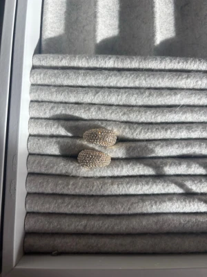 Guldiga örhängen med små pärlor - Snygga guldiga örhängen i rundad form, täckta med små vita pärlor som ger ett lyxigt och glittrande intryck. Perfekta för dig som vill ha något elegant och trendigt. Örhängena har en klassisk creol-design och stängs med smidig klämma.