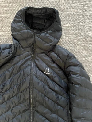 Svart dunjacka med huva från Haglöfs - Säljer en svart dunjacka från Haglöfs med huva och dragkedja framtill. Storlek L men passar mindre också! Perfekt till våren men passar lika bra på vintern🤩