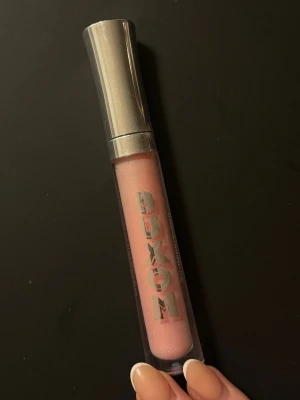 Buxom Kimberly ljusrosa läppglans - Säljer ett Buxom läppglans i nyansen Kimberly, en ljusrosa färg med subtilt skimmer. Förpackningen är genomskinlig med silvrigt lock och stor BUXOM-logga på tuben. Perfekt för dig som vill ha glansiga och fylliga läppar.