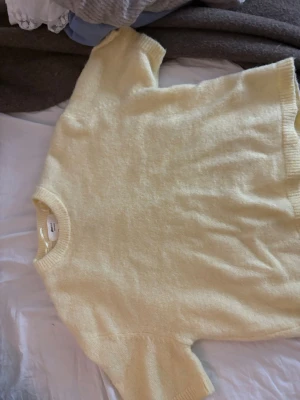 Gul stickad tröja från Gina Tricot - Mysig ljusgul stickad tröja från Gina Tricot i ullblandning. Tröjan har korta ärmar, rund halsringning och ribbade kanter. Perfekt för lager på lager och en fräsch look till vardagsoutfiten.