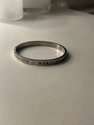 Silverfärgat armband med stenar - Snyggt och stilrent armband i silverfärgad metall med infattade klara stenar runt hela bandet. En sten är av men inget man tänker på! Fint skick och pris kan diskuteras 💞