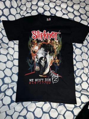 Slipknot svart band t-shirt - Säljer en svart Slipknot t-shirt med tryck av bandets logga och motiv på framsidan samt autograf-liknande tryck på baksidan. T-shirten har korta ärmar och är gjord i bomull. Perfekt för dig som gillar metal och vill sticka ut.