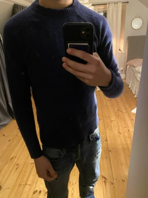 Blå  stickad tröja - Mysig mörkblå stickad tröja med rund halsringning och långa ärmar. Tröjan har ribbstickade muddar vid ärmslut och nederkant. Perfekt för kyligare dagar och enkel att matcha med jeans eller andra byxor. Nypriset är 500 och säljer för den blivit lite liten men inga defekter eller något annat. Priset kan diskuteras vid snabb affär
