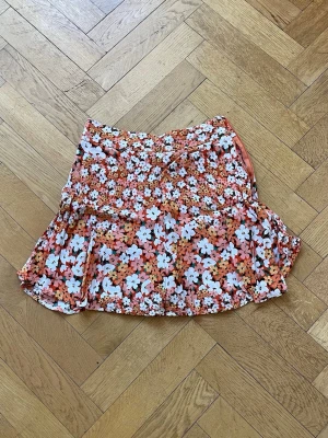 Blommig volangkjol i orange och vitt - Kort byx-kjol med orangea o vita blommor.