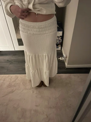 Vit långkjol från Gina Tricot - Supersnygg vit långkjol från Gina Tricot med bred smock i midjan och volangdetalj nedtill. Fint skick och pris kan diskuteras 💞.