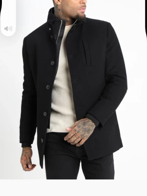 Rock ifrån Jack & Jones  - Snygg svart rock med ståkrage och knäppning framtill. Rocken har en stilren design med diskreta fickor och en bröstficka. Perfekt för dig som vill ha en tidlös och clean look. Köpt på Jack & Jones. Nypris 1595kr