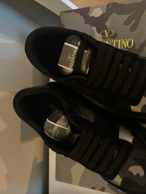 Valentino camo sneakers svart/grön - Snygga sneakers från Valentino i svart och grönt camomönster. Skorna har svarta snören, detaljer i mocka och textil samt logga på plösen. Perfekta för dig som vill sticka ut med exklusiva och trendiga sneakers.